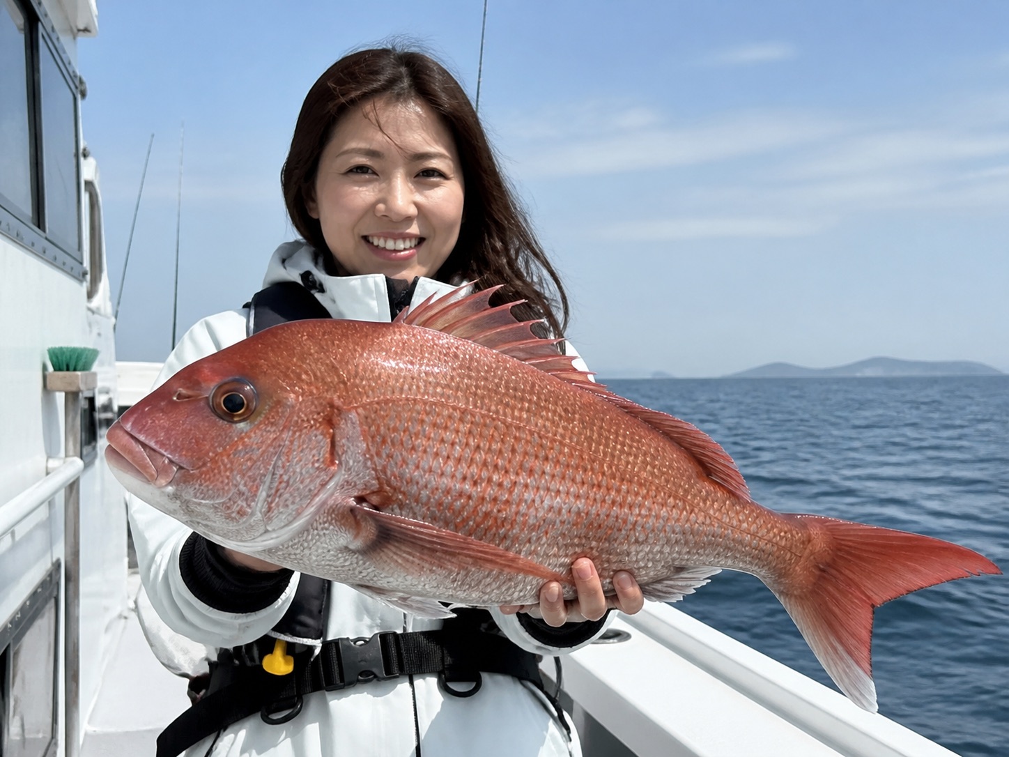 船上で大きな真鯛を持つ女性の釣り人